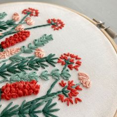 a close up of a embroidery on a white cloth with red flowers and green leaves