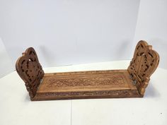 a wooden bench with carved carvings on the back and sides, sitting against a white wall