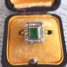 an emerald and diamond ring in a velvet case on top of a piece of paper