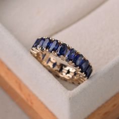 a gold ring with blue sapphires in it sitting on top of a white box