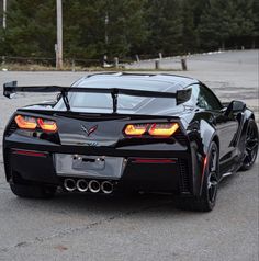 the rear end of a black sports car parked in a parking lot next to trees