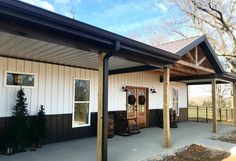 a covered porch with chairs and trees in the back ground, next to a white building