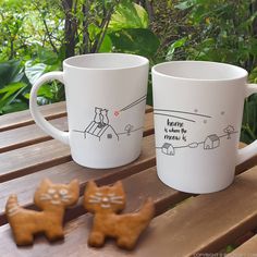 two coffee mugs sitting on top of a wooden table next to small ginger cookies