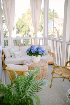 a living room with wicker furniture and blue flowers on the coffee table in front of it