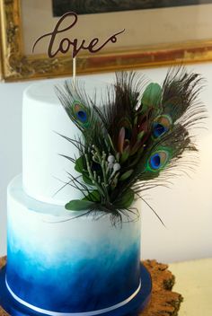 there is a blue and white cake with feathers on the top, next to a sign that says love