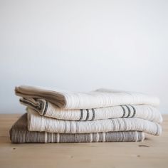 three folded towels sitting on top of a wooden table next to a white wall and wood floor