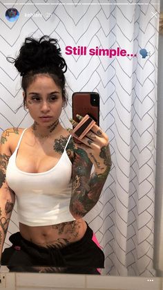 a tattooed woman taking a selfie in front of a mirror with her cell phone