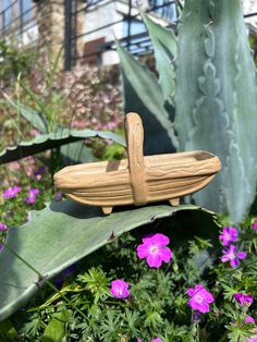 a wooden toy boat sitting on top of a green leafy plant next to purple flowers