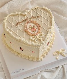 a heart shaped cake sitting on top of a white tablecloth covered bed sheet with an ornament in the shape of a cage