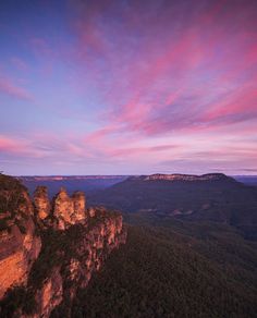 the blue mountains are covered in pink and purple clouds as the sun sets over them