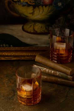 two glasses filled with liquid sitting on top of a table next to books and a painting