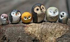 five small ceramic owls sitting on top of a tree stump with one looking at the camera