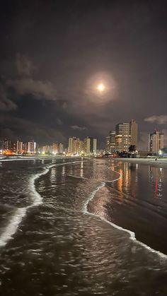 the moon is setting over the beach and city lights are reflected in the wet sand