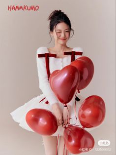 a woman in a white dress holding red balloons