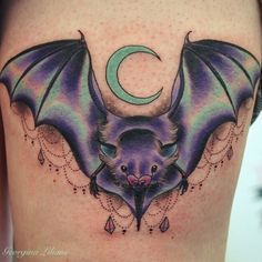 a bat tattoo on the side of a woman's thigh with a crescent moon behind it