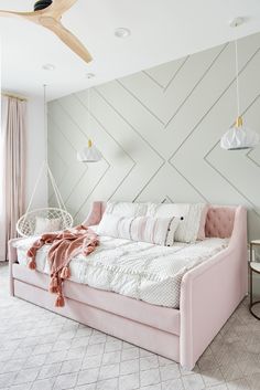 a pink daybed with pillows and blankets on it in front of a white wall