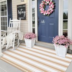 the front porch is decorated for spring with pink flowers in white planters and a blue door