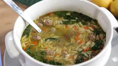 a white bowl filled with pasta and meat soup on top of a table next to lemons