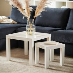 two white tables sitting on top of a carpeted floor next to a blue couch