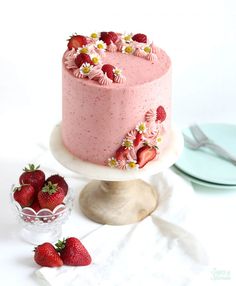 a pink cake with strawberries and daisies on top