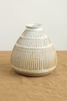 a white vase sitting on top of a wooden table next to a brown cloth covered floor