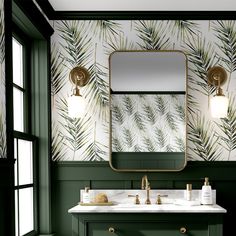 a green bathroom with palm leaves on the wall and gold faucet lights above it