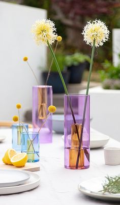 three vases filled with yellow flowers sitting on top of a white table covered in plates