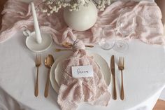 a white table topped with pink napkins and silverware next to a vase filled with baby's breath flowers