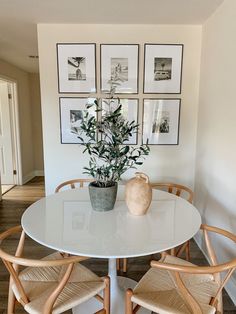 a white table with four chairs and a potted plant on it in front of framed pictures