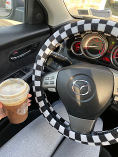 the steering wheel cover is decorated with black and white checkered fabric, along with a cup of coffee