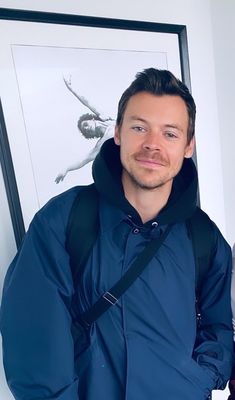 a man with a backpack standing in front of a framed photo and smiling at the camera