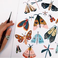 a person holding a pencil in front of an open book with butterflies on it and dragonflies