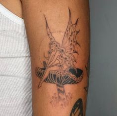 a woman's arm with a tattoo on it that has an image of a fairy sitting on top of a mushroom