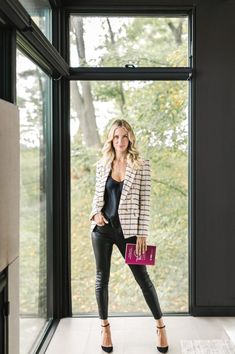 a woman standing in front of a window holding a pink purse and looking at the camera