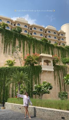 a woman standing in front of a building with plants growing on it's side