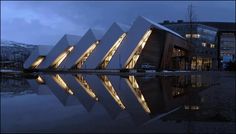 a building that has some lights on it in front of a body of water with mountains in the background