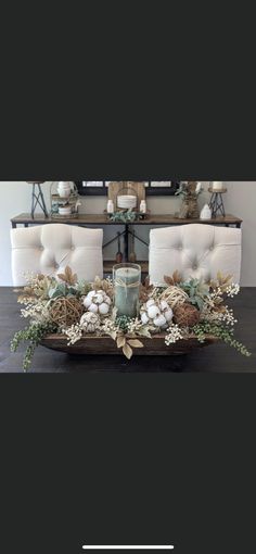 an arrangement of flowers and candles on a table in front of two couches with white cushions