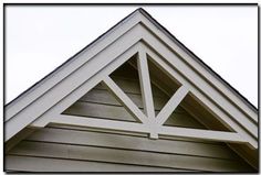 the corner of a house with a roof made of wood and white trim on it