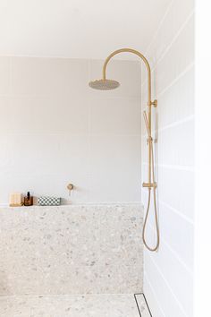 a white bathroom with a gold shower head and hand held shower faucet in the corner