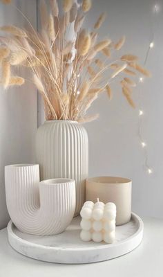 a white vase sitting on top of a table next to candles and some plants in it