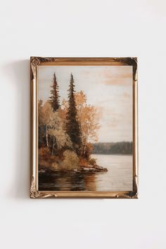 a painting hanging on the wall next to a white wall with a brown frame and trees