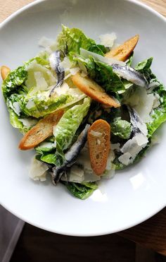 a white bowl filled with lettuce and fish on top of a wooden table