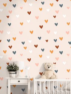 a teddy bear sitting next to a crib with hearts on the wall behind it