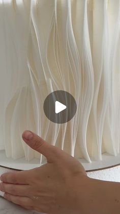 a hand is pointing at an object that looks like wavy white paper and has a video screen in front of it