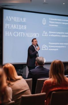 a man standing in front of a projection screen giving a presentation to people sitting on chairs