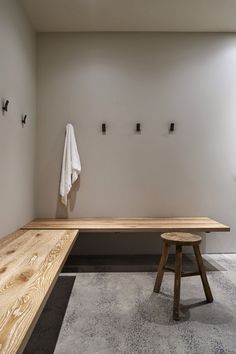 a wooden bench sitting next to a white wall with hooks on it's side