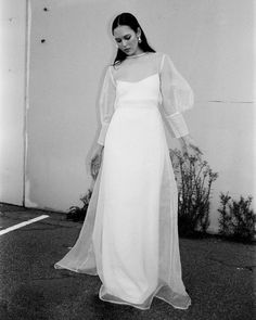 a black and white photo of a woman in a long dress with sheer sleeves on