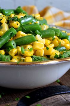 a white bowl filled with green beans and yellow corn on top of a wooden table