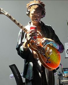 a person with headphones on holding an electric guitar in front of a computer desk