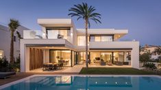 a house with a swimming pool in front of it at dusk, surrounded by palm trees